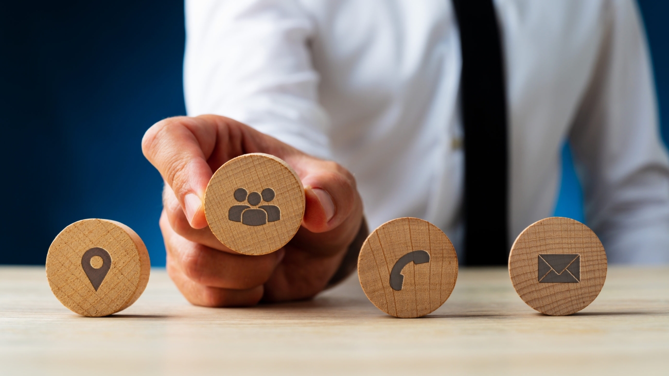 Business customer service representative placing four wooden cut circles with contact and information icons on them in a row.