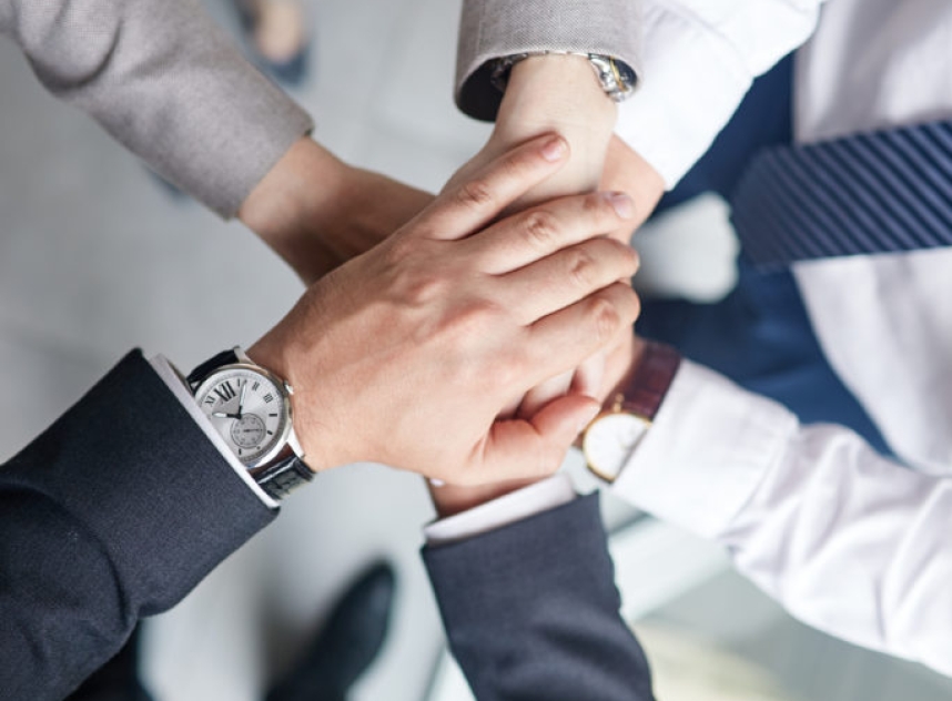 Group of colleagues in formalwear joining hands together while celebrating completion of joint project, close-up shot